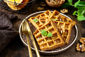 Homemade pumpkin waffles with walnuts in a plate on a brown culinary background closeup
