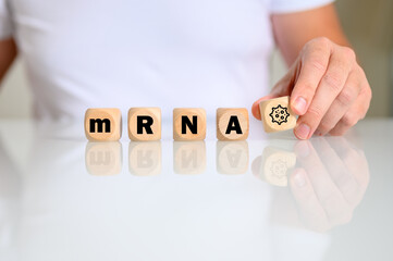 Frau am Schreibtisch legt aus Buchstaben das Wort mRNA mit dem Symbol eines Virus