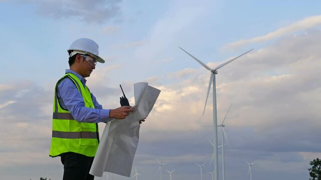Young male engineer analyze a blueprint drawing of wind turbine farm.
