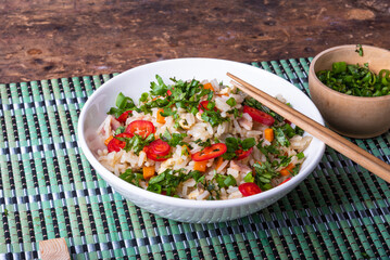 Stir fry rice with pork and vegetables and chopped hot peppers and herbs in a bowl with chopsticks