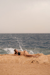 Pretty woman posing in the sea. Young caucasian woman in black swimsuit and golden dress sitting on stone shore