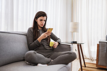 Happy Latin lady relax at home alone sit on room pose share good news at social media via cellphone. Smiling mixed race woman enjoy weekend order goods food online in phone app. Home office.