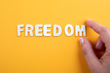 FREEDOM. Word from white letters with a woman's hand on yellow background