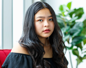 Front view portrait shot of a beautiful smiling young junior teenager in a black dress sitting on...