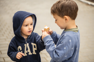 two brothers are eating one ice cream on the street. Boy takes ice cream with his brother