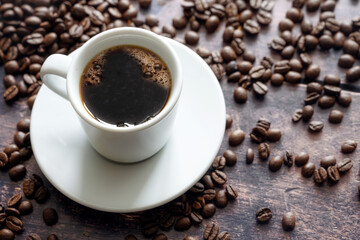 White cup with strong black coffee on a rustic wooden table with some beans, copy space, selected...