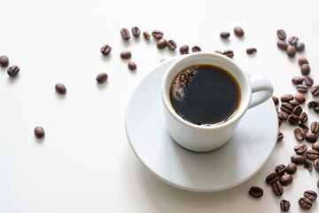 Hot coffee, black and strong in a white cup on a bright table with some beans, copy space, selected focus