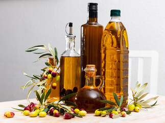 Decanters and bottles with golden olive oil garnished with ripe olives on wooden surface
