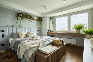 Stylish bedroom interior in modern apartment with small bed, wooden chest, home garden, white...