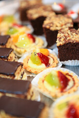 Close up of assorted fruit desserts and chocolate cake bites in tray on table with bokeh background. Catering service. No people. Selective focus. 