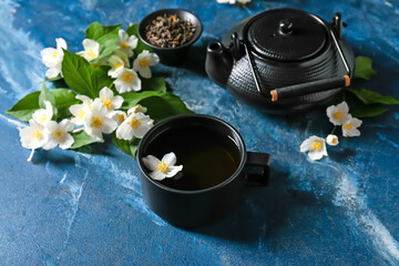 Cup of jasmine tea, teapot and flowers on color background