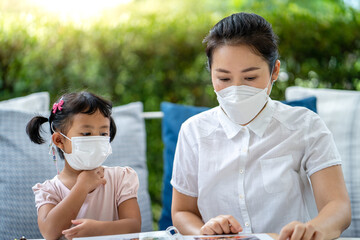 Young mother and little girl wearing protective face mask  sitting at restaurant.