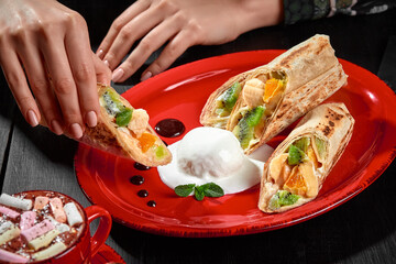 Female hand holding sweet fruit roll in lavash served with ice cream