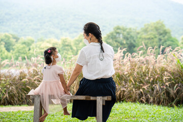 Obraz premium young mother and daughter with protecting face mask sitting at park.