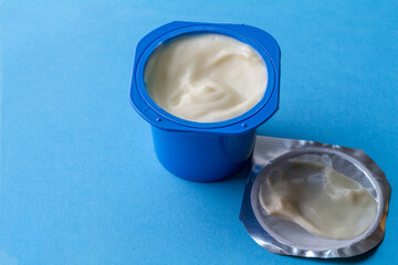 Yogurt cup with creamy yoghurt in blue pot and foil lid isolated on blue background with copy space