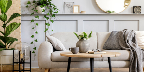 Scandinavian living room interior with design grey sofa, wooden coffee table, tropical plants, shelf, mirror, furniture, plaid pillow, teapot, book and elegant personal accessories in home decor.