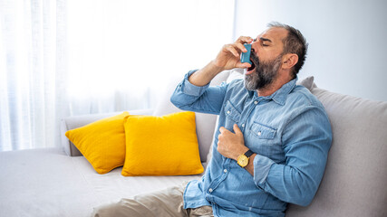 Fototapeta premium Portrait of a man with an asthma inhaler in his hands, an asthmatic attack. The concept of treatment of bronchial asthma, cough, allergies, dyspnea. Man using an asthma pump