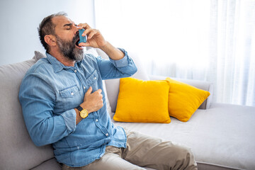 Man using asthma inhaler. Man using asthma inhaler for relief an attack at home for preventing attack. Man using medical inhaler to prevent and treat wheezing and shortness of breath.