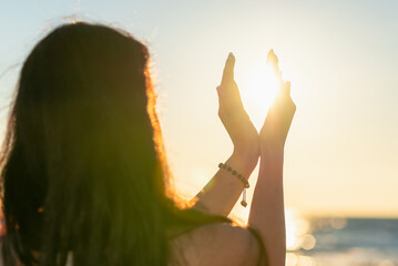 Silhouette of young woman's hands relaxing, happy meditating and holding sunset against golden hour...