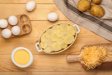 Preparing of tasty potato casserole in baking dish on wooden background