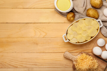Preparing of tasty potato casserole in baking dish on wooden background