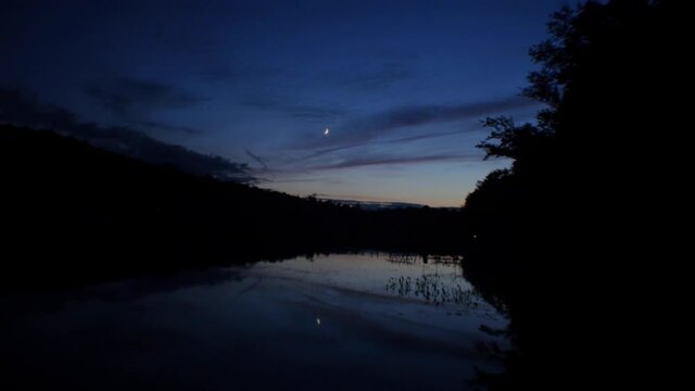 Crescent moon reflected on lake at dusk