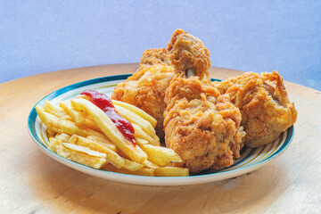 Plate with several fried chicken leg and fries on a wooden background. Side view