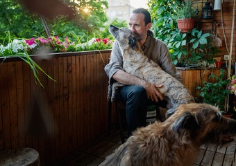 Attractive mature middle aged man sitting with his two dogs at home on summer balcony. Love for pets