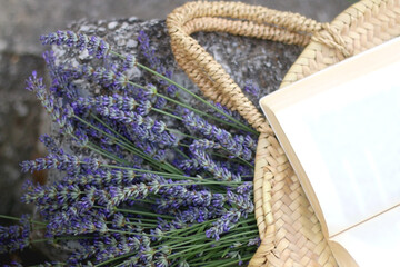 Straw bag filled with fresh lavender flowers and open book. Flat lay.