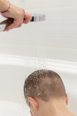preschooler boy washes in a light white bathroom at home. water pours on top of his head from the shower head