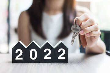 Young Businesswoman hands holding key and 2022 Happy New Year with house model on table office. New...