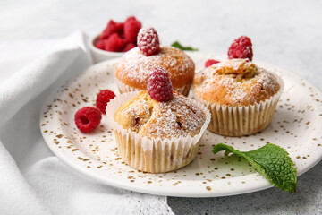 Plate with tasty raspberry muffins on light background, closeup