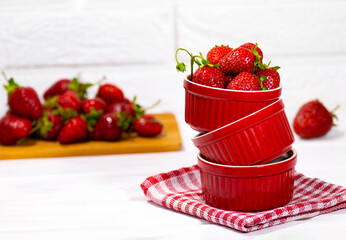 Juicy Fresh Strawberries in a Balance Red Bowl on a piece of cloth on a white Brick background. Vitamin food. Copy space. Strawberry on wooden Desk.