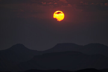 Naklejka premium incredible view of setting sun above mountains in africa during sunset, red sky