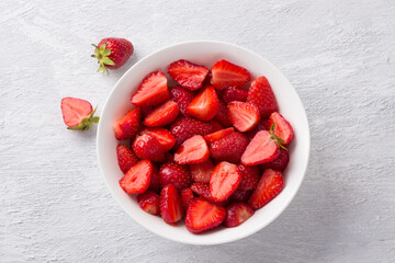 White bowl with fresh chopped strawberries on a light gray background