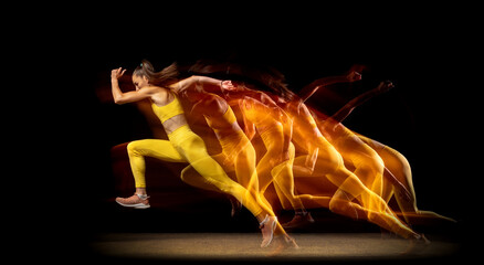 Young woman, female athlete running aside isolated over black studio background in mixed neon...