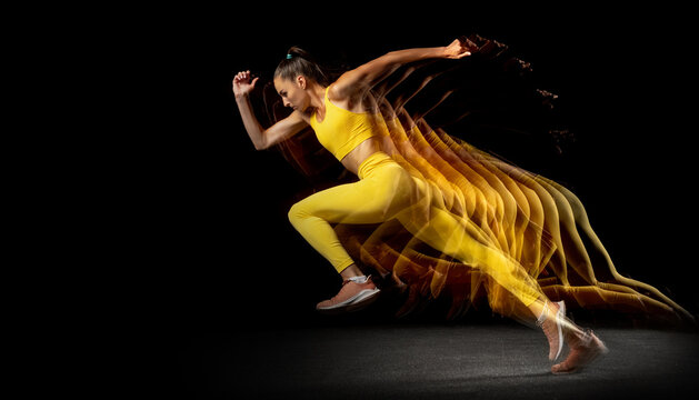 Young professional female athlete running aside isolated over black studio background in mixed neon lights. Side view