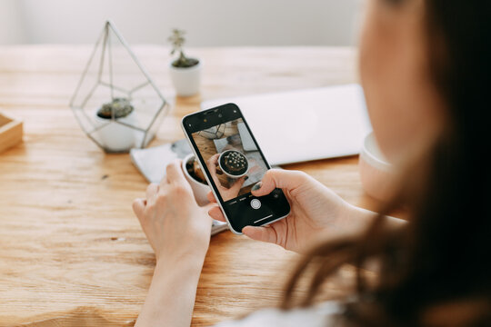A young woman photographer blogger makes content creates flatlay photos on the desktop using a camera and a mobile phone in a home office, selective focus