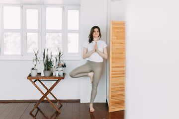 A athletic healthy young woman in sportswear does sports as a yogi does a workout stretching and meditates sitting in a pose near plants at home, selective focus