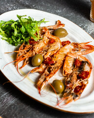 Fried langoustines served with olives and salad leaves. Grilled tasty langoustines on a white oval plate. Restaurant serving, horizontal orientation.