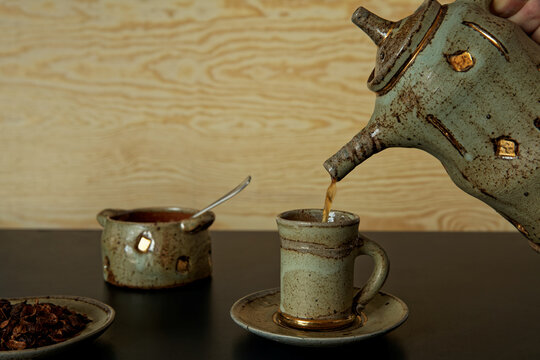 Pouring cascara beverage in unique ceramic teapot to tea cup.