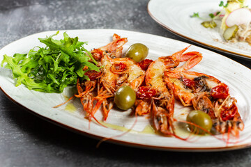 Fried langoustines served with olives and salad leaves. Grilled tasty langoustines on a white oval plate. Restaurant serving, horizontal orientation.