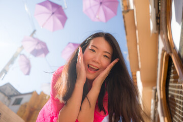 outdoors urban lifestyle portrait of young happy and attractive Asian Korean woman on street full of hanging umbrellas during summer holidays travel in Europe