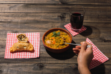 Typical Argentinean food locro and empanadas on a wooden background.