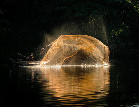 Two fishermen in a boat casting a fishing net into river, Vietnam