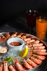 Royal shrimp on ice. A plate with cold fresh prawns, ice, lemon, lime and sauce. Sea buckthorne morse on the table. Low key. Vertical orientation.