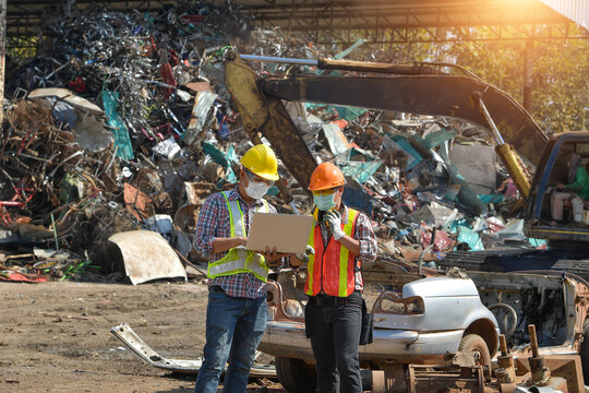 Two workers looking at a laptop at a scrap metal yard, Thailand