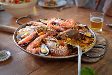 Appetizing seafood paella in pan against beer on table
