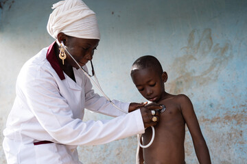 Black nurse auscultating a small attentive African boy's chest with a stethoscope to check out for...