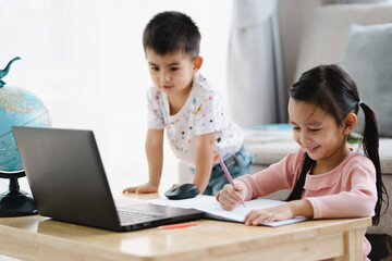 Happy asian schoolgirl is happy learning for online class nearly with little brother in the living...